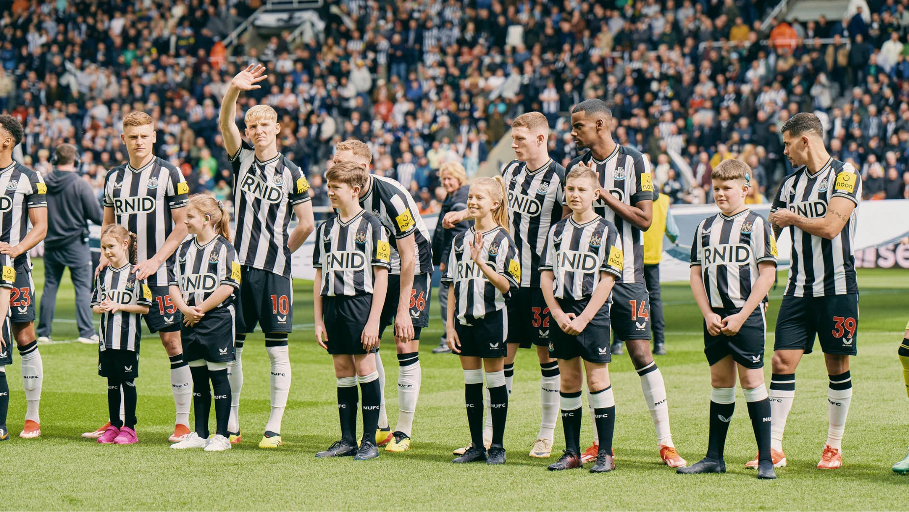 Newcastle United footballers and children lined up on the pitch in front of the crowd at St James’ Park